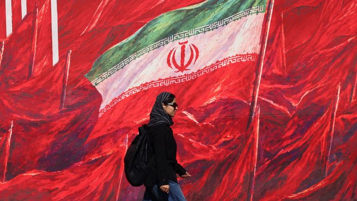 A woman walks past a mural bearing Iran’s national flag in Tehran, 26 October 2026 (Atta Kenare AFP)